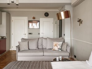 Een kamer in neutrale tinten met een bank, een bed, een lamp en een wandklok.