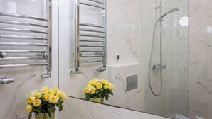 Une salle de bain moderne avec une douche à parois de verre, des porte-serviettes en chrome et un miroir agrémenté d’un arrangement floral.