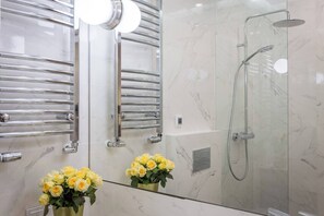 Ein modernes Badezimmer mit einer gläsernen Duschkabine, chromfarbenen Handtuchhaltern und einem Spiegel mit Blumenarrangement.