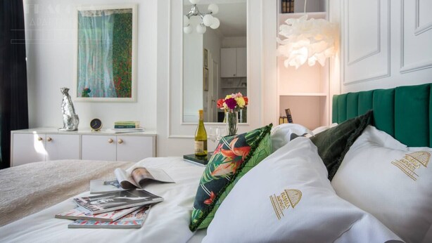 Une chambre d’hôtel bien rangée, avec un lit, une table de chevet dotée d’une lampe, un miroir et un tableau accroché au mur.