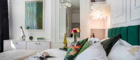 A neatly arranged hotel room with a bed, a bedside table with a lamp, a mirror, and a painting on the wall.