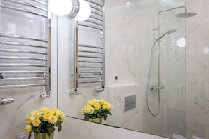 A modern bathroom with a glass-enclosed shower, chrome towel racks, and a mirror with a flower arrangement. - Feniks Smaragd studio - no view (Kraków - Feniks)