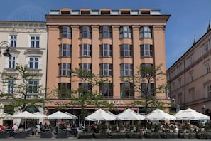 A multi-story hotel with a central entrance, outdoor seating area with umbrellas, and a clear sky. - Feniks Smaragd studio - no view (Kraków - Feniks)