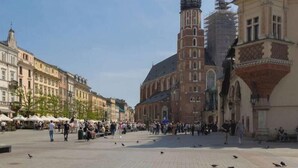 Une place publique bordée de bâtiments historiques, dominée par une tour imposante, et offrant une vue sur un ciel dégagé.