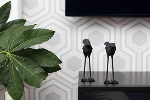 En stor, grön växt, två svarta skulpturer formade som fåglar och en tv-apparat på en vägg med ett geometriskt mönster.