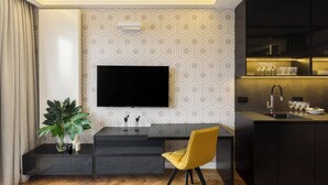 Una cocina moderna con televisor integrado, un área de comedor con una silla amarilla y una planta en maceta.
