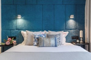 A bed with a blue headboard, multiple pillows, a bedside table with a candle, and a nightstand with a lamp. - Studio Feniks Exceptional with terrace (Kraków - Feniks)