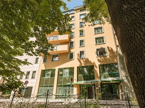 A multi-story building with a green awning, large windows, and a tree in the foreground. - Apartment Serene 3-bed (Kraków – Old Town)