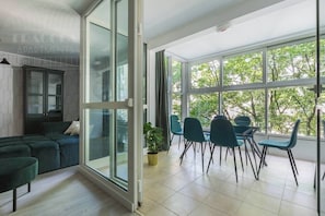 Una sala moderna con un sofá, un comedor con sillas y un ventanal con vistas a árboles.