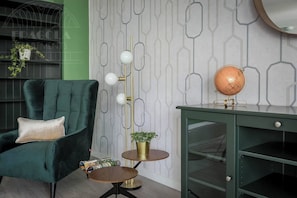 Una habitación con un sillón verde, un globo terráqueo sobre un escritorio, una lámpara de pie y un papel tapiz estampado.