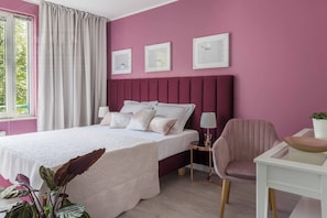 A bedroom with a bed, a chair, a table, and a window with curtains. - Apartment Serene 3-bed (Kraków – Old Town)