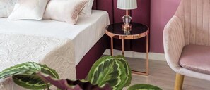 A neatly made bed with a white duvet, a small round table with a lamp, and a chair with a cushioned seat.