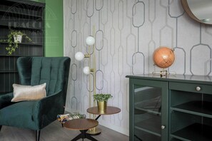 A room with a green armchair, a globe on a desk, a floor lamp, and a patterned wallpaper. - Apartment Serene 3-bed (Kraków – Old Town)