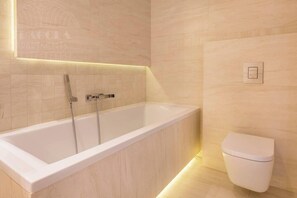 A modern bathroom with a freestanding bathtub, a toilet, and a wall-mounted light fixture. - Apartment Serene 3-bed (Kraków – Old Town)