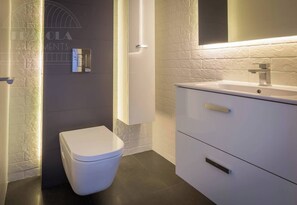 A modern bathroom with a white toilet, a sink with a mirror above it, and a wall-mounted light fixture. - Apartment Serene 3-bed (Kraków – Old Town)