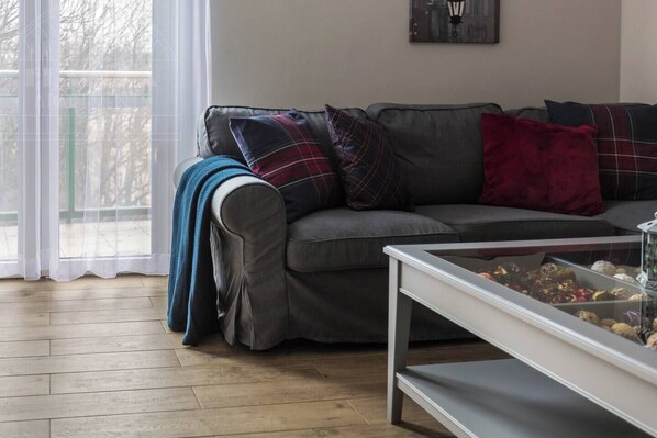 A living room with a grey sofa, a glass coffee table, and a view of a balcony.