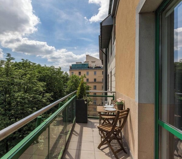 A balcony with a table and chairs, a potted plant, and a view of buildings and trees.