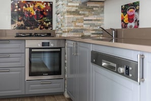 Una cocina con armarios grises, horno Bosch, lavavajillas y protector de pared de piedra.