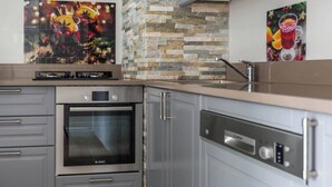 Una cocina con armarios grises, horno Bosch, lavavajillas y protector de pared de piedra.