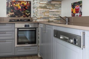 A kitchen with grey cabinets, a Bosch oven, a dishwasher, and a stone backsplash. - Homely 1-bedroom apartment (Kraków – Old Town)