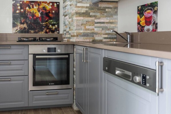 A kitchen with grey cabinets, a Bosch oven, a dishwasher, and a stone backsplash.