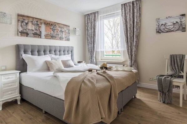 Un dormitorio con una cama grande, una mesita de noche, una silla, un ventanal con cortinas y decoración en la pared.