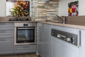 Een koelkast, een kookplaat, een vaatwasser, kookgerei, borden en bestek