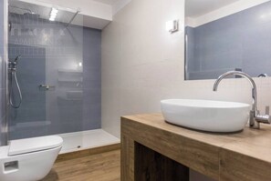 Un baño moderno con ducha envuelta en vidrio, un lavamanos blanco y un mueble de tocador de madera.