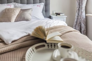 A neatly made bed with a book, a cup, and a tray with a teapot.