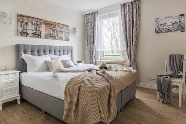 Un dormitorio con una cama grande, una mesita de noche, una silla, un ventanal con cortinas y decoración en la pared.