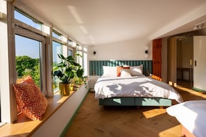 Un dormitorio con cama, ventanas amplias, una planta en maceta y vistas al verdor.