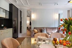 A modern living room with a glass dining table, a sofa, and a kitchen in the background.