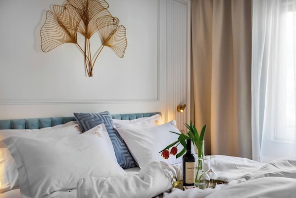 A neatly made bed with white and blue pillows, a decorative wall piece, and a bedside table with a bottle and glass.