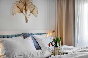 Uma cama bem arrumada com travesseiros brancos e azuis, um objeto decorativo na parede e uma mesinha de cabeceira com uma garrafa e um copo.