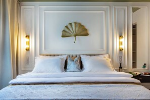 Cama bem arrumada com lençóis brancos, arte de parede decorativa com conchas e duas luminárias fixadas na parede.