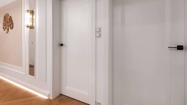 A hallway with white doors, a light fixture, and a wall-mounted decoration.