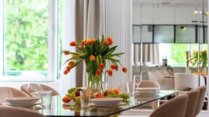 A dining area with a glass table, chairs, a vase of tulips, and a view of greenery outside.