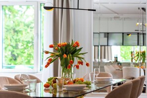 A dining area with a glass table, chairs, a vase of tulips, and a view of greenery outside.