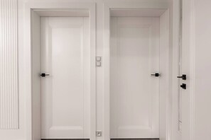 Two white doors with black handles, a light switch, and a power outlet on the wall.