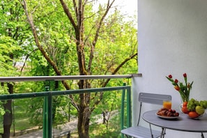 Uma varanda com mesa posta para o café da manhã, um vaso com flores e vista para árvores verdejantes.