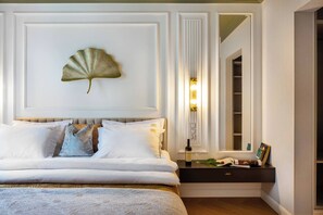 Une chambre à coucher avec un lit, des oreillers, une table de chevet avec une bouteille et un verre, un ventilateur fixé au mur et un miroir.
