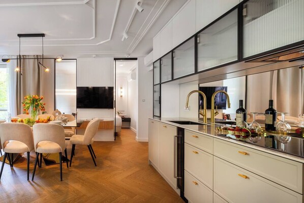 A modern kitchen with a built-in oven, a stainless steel sink, and a dining area with a table and chairs. - Apartment Ivory Dream (Kraków – Old Town)