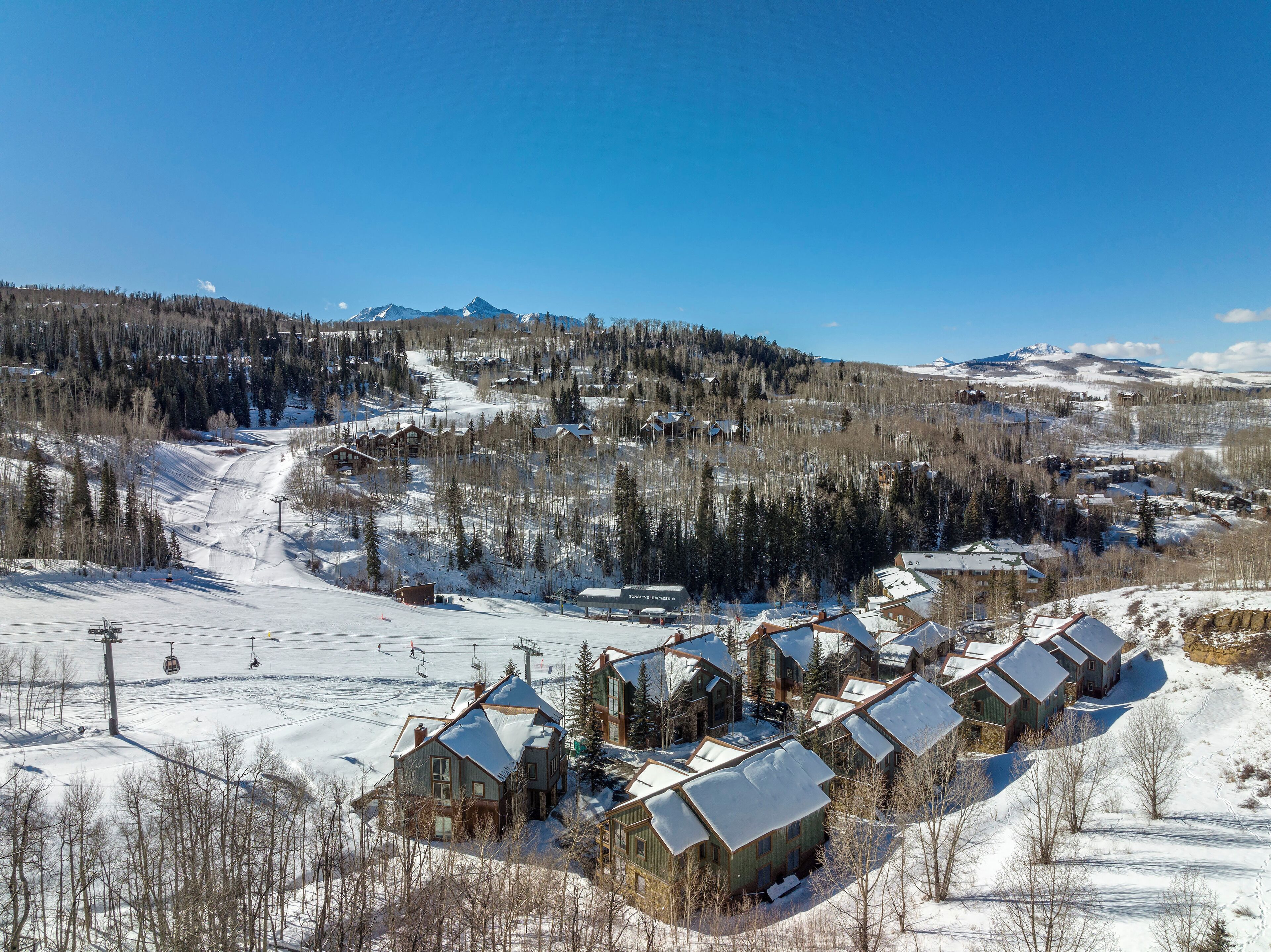 A snow-covered mountain resort with multiple chalet-style buildings, ski lifts, and a ski slope.