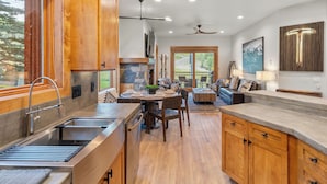 A modern kitchen with wooden cabinets, a stone fireplace, and a dining area with a round table and chairs. - Terraces A+ TRUE Ski-In Ski-Out 2 Bedroom, 2 Bathrooms - Sleeps 4 (Mountain Village)