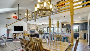 A spacious living area with a wooden dining table, multiple chairs, a chandelier, and a stone fireplace. - Hot Tub + Fire Pit: Possum Kingdom Lake Retreat! (Caddo)