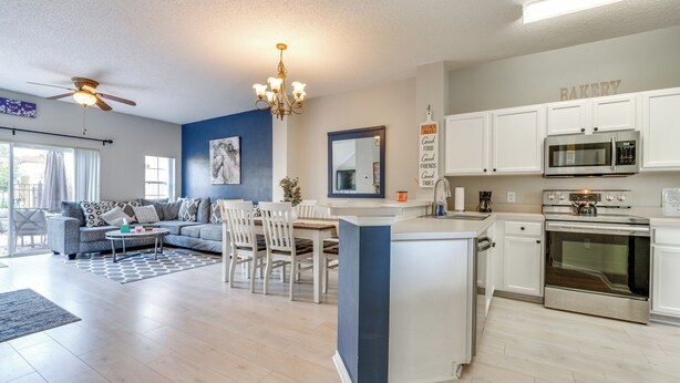 A modern kitchen with white cabinets, a built-in microwave, and an oven. There is a dining area with a table and chairs.