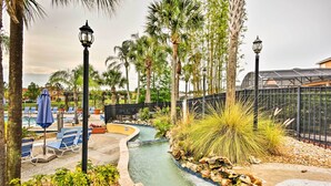 A pool area with lounge chairs, a water feature, palm trees, and a fence.