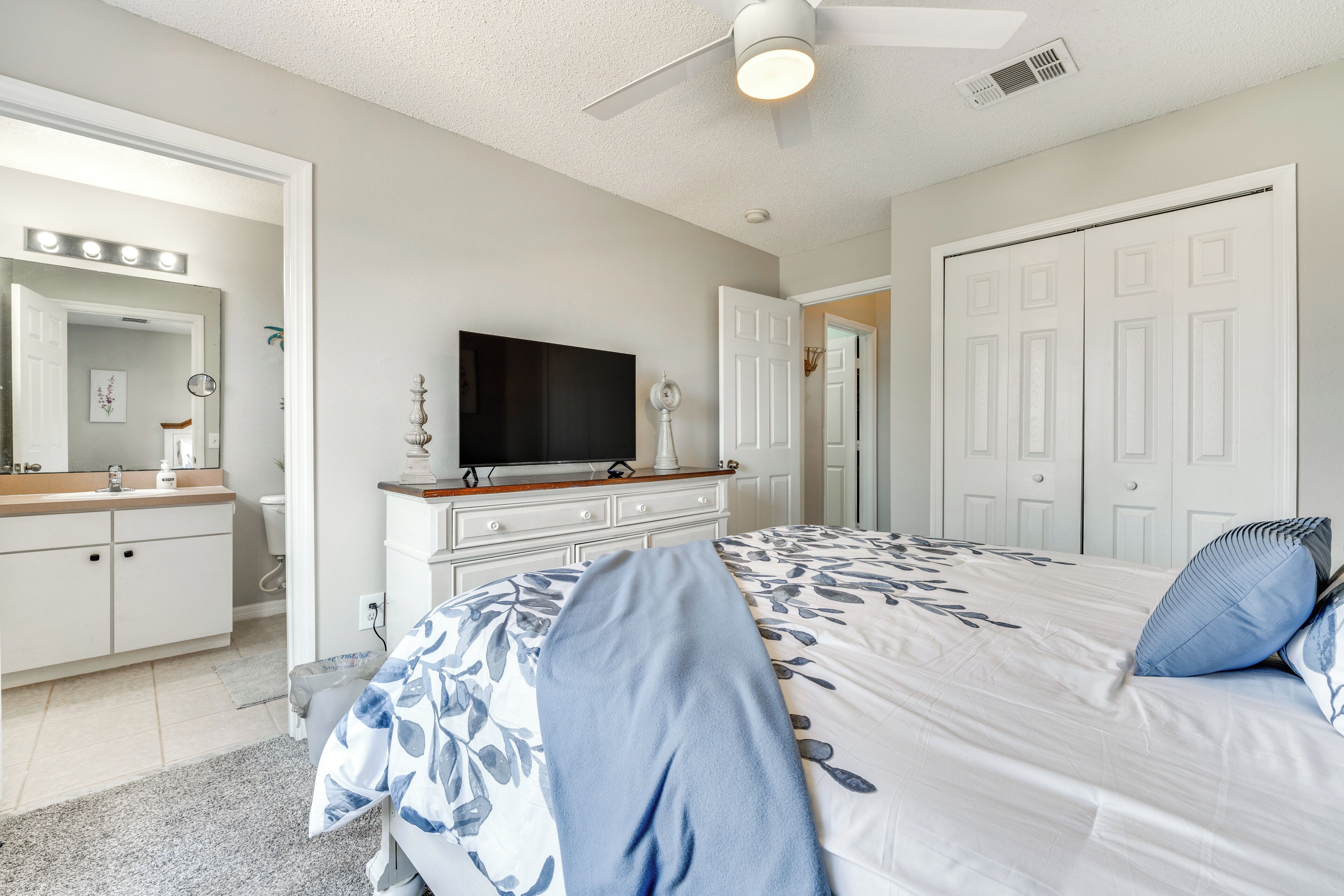 A bedroom with a bed, dresser, vanity, and a television.