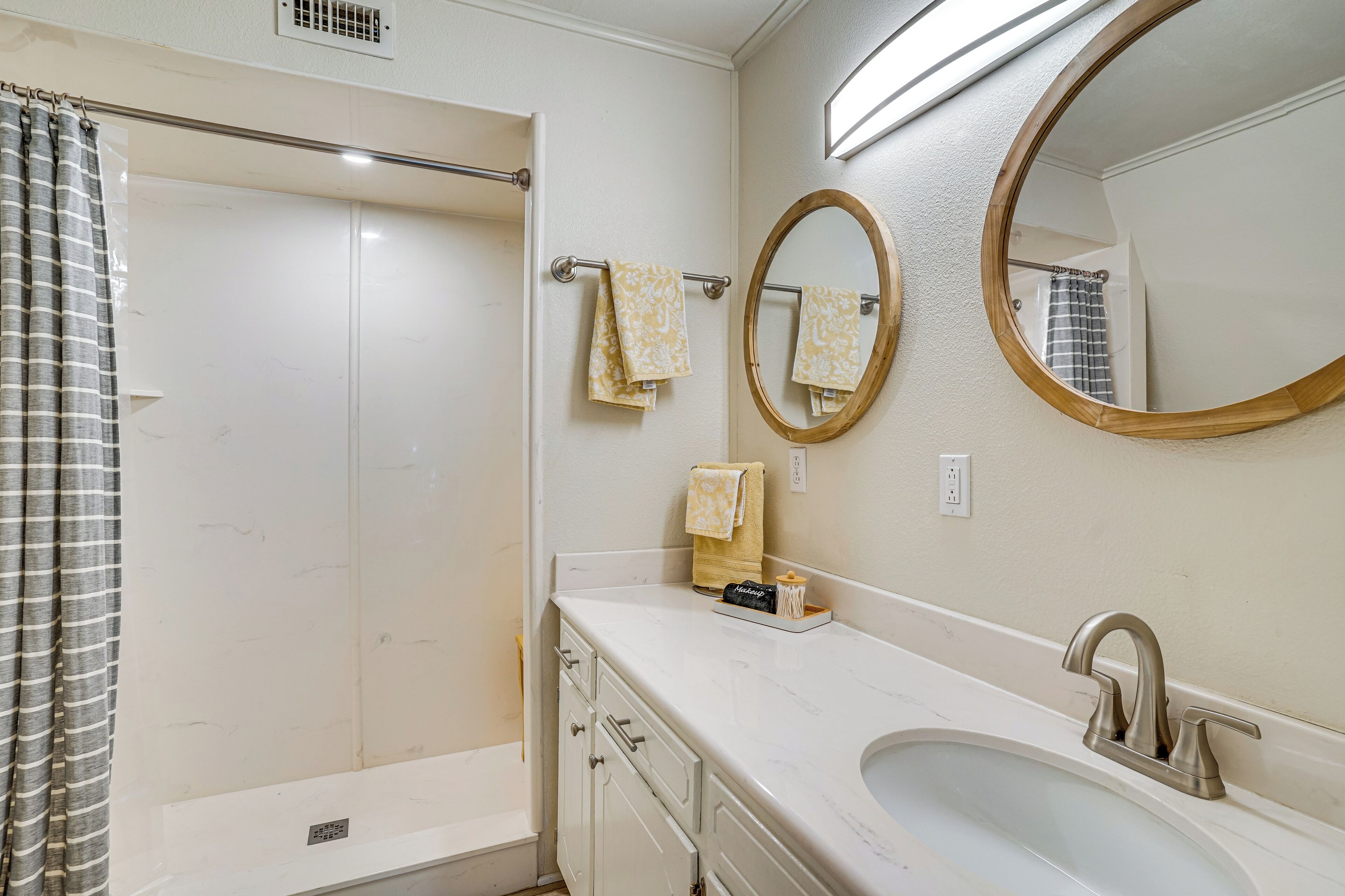 A bathroom with a shower, a sink, a mirror, and towels.