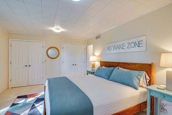 Un dormitorio con cama, mesita de noche, lámpara y un cartel que dice 'NO WAKE ZONE', además de una puerta.